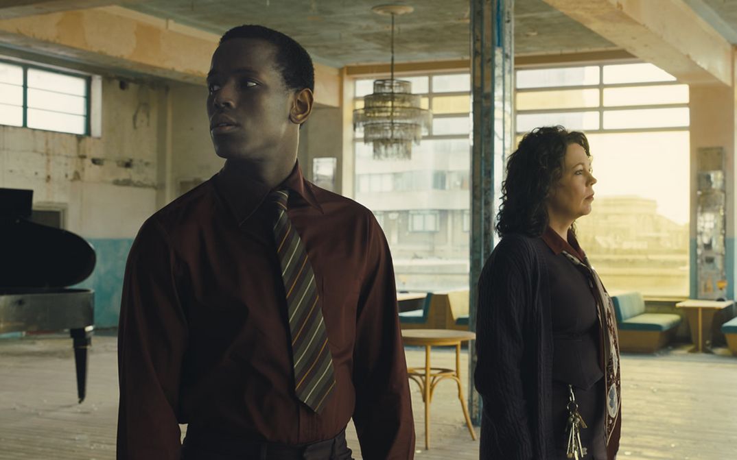 Filmstill aus EMPIRE OF LIGHT: Ein Mann und eine Frau stehen in einem großen, verlassen wirkenden Raum und blicken sich um. Im Raum sind Tische und Bänke und ein Flügel zu sehen.