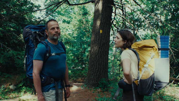 Film still from GOOD ONE: A teenage girl and her father are standing in the forest with large hiking rucksacks.