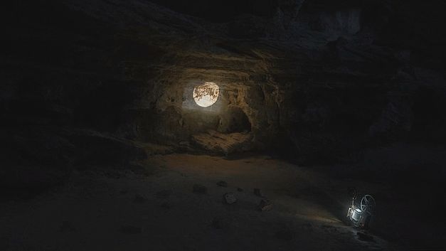 Filmstill aus dem Film „QUEBRANTE“ von Janaina Wagner. Bilder des Mondes werden auf eine Höhlenwand projiziert, wobei die Projektion die einzige Lichtquelle ist.