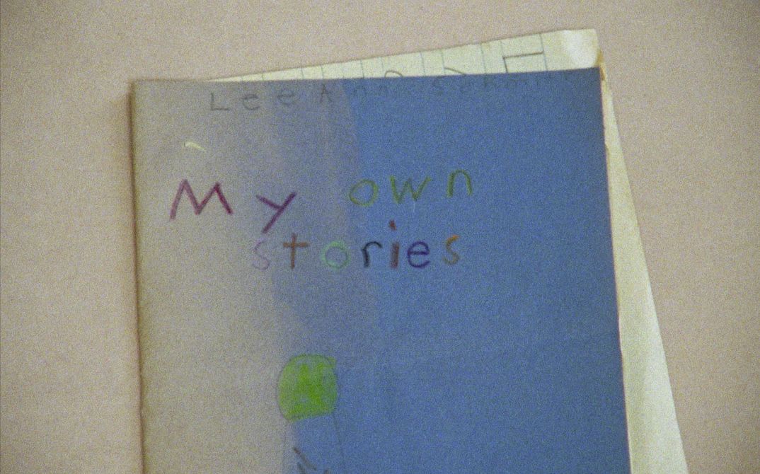 Film still from EVIDENCE by Lee Anne Schmitt. The picture shows a blue exercise book with a child