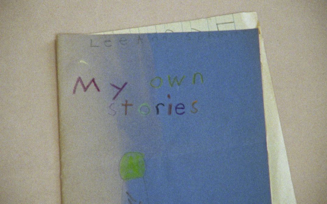 Film still from EVIDENCE by Lee Anne Schmitt. The picture shows a blue exercise book with a child