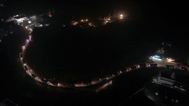 Nachtaufnahme einer kurvigen Straße mit Fahrzeuglichtern aus der Luft.