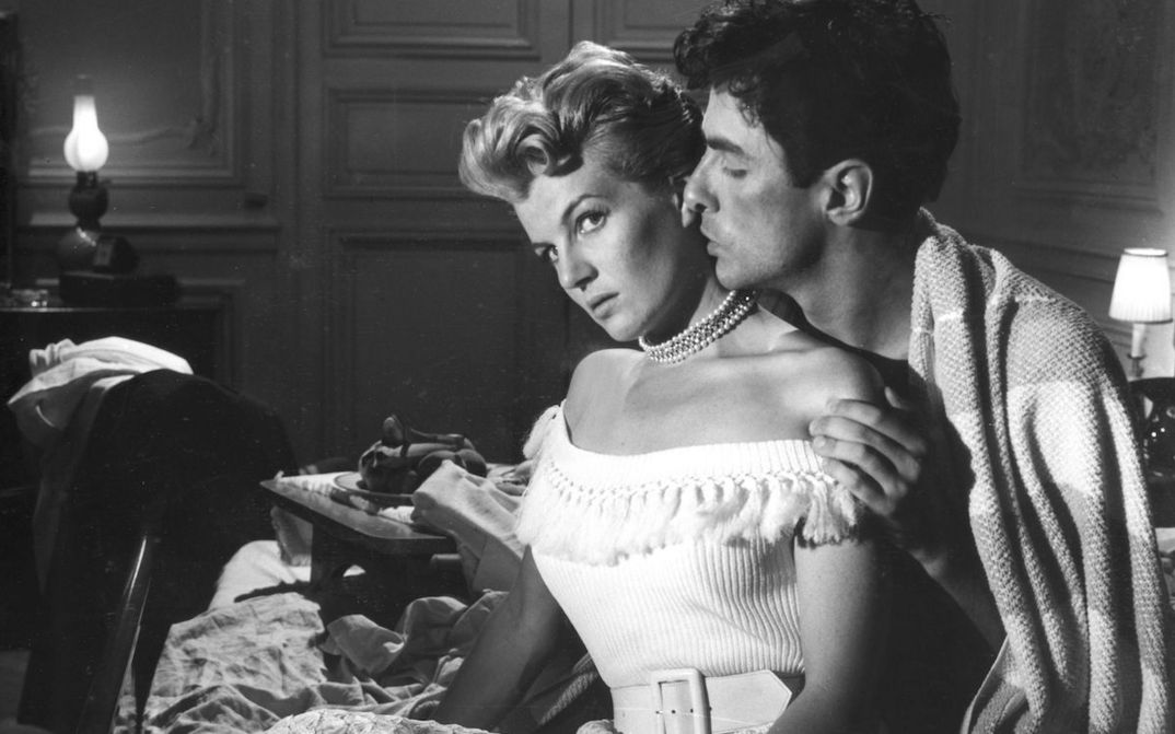 Filmstill aus LE RAGAZZE DI SAN FREDIANO: Ein Mann und eine Frau sitzen angezogen am Bettrand. Er sitzt hinter ihr und küsst sie auf den Hals.