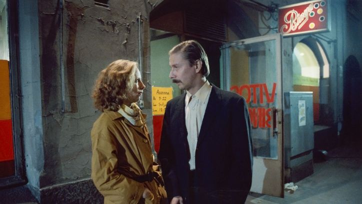 Filmstill aus SCHATTEN IM PARADIES: Ein Mann und eine Frau blicken sich an, hinter ihnen die beleuchtete Anzeige eines Nachtlokals.