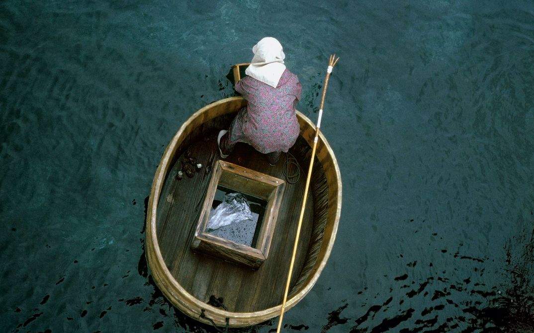 Filmstill aus UNTER SCHNEE: Man sieht von oben aufgenommen eine Person in einem winzigen Boot auf einem Gewässer beim Fischen.