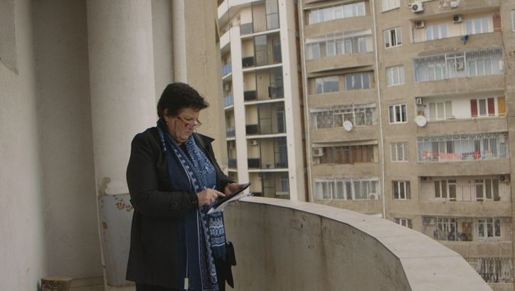 Filmstill aus SUNNY. Auf dem Balkon eines Hauses blickt eine Frau auf ein Tablet in ihrer Hand.