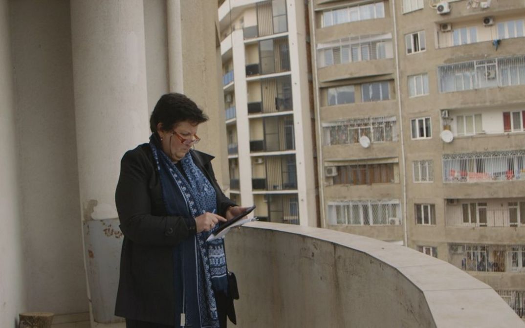 Filmstill aus SUNNY. Auf dem Balkon eines Hauses blickt eine Frau auf ein Tablet in ihrer Hand.