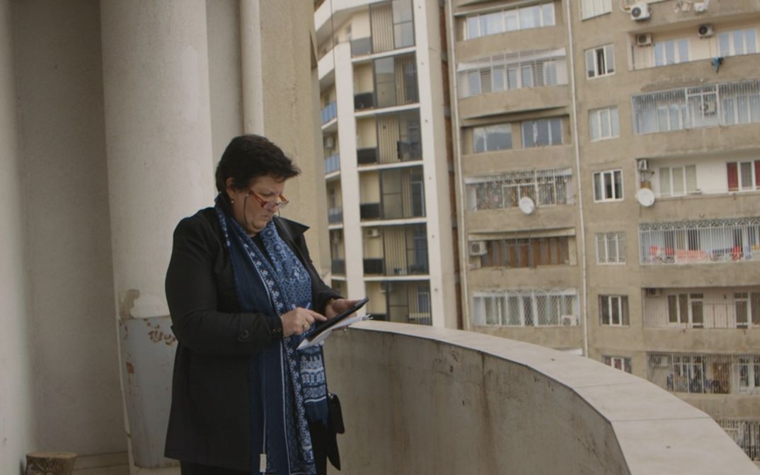 Filmstill aus SUNNY. Auf dem Balkon eines Hauses blickt eine Frau auf ein Tablet in ihrer Hand.
