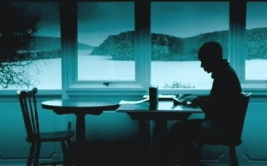 Film still from DIGITOPIA: You can see the greenish monochrome image of a man sitting at a table by a large window. A hilly landscape can be seen behind the window.