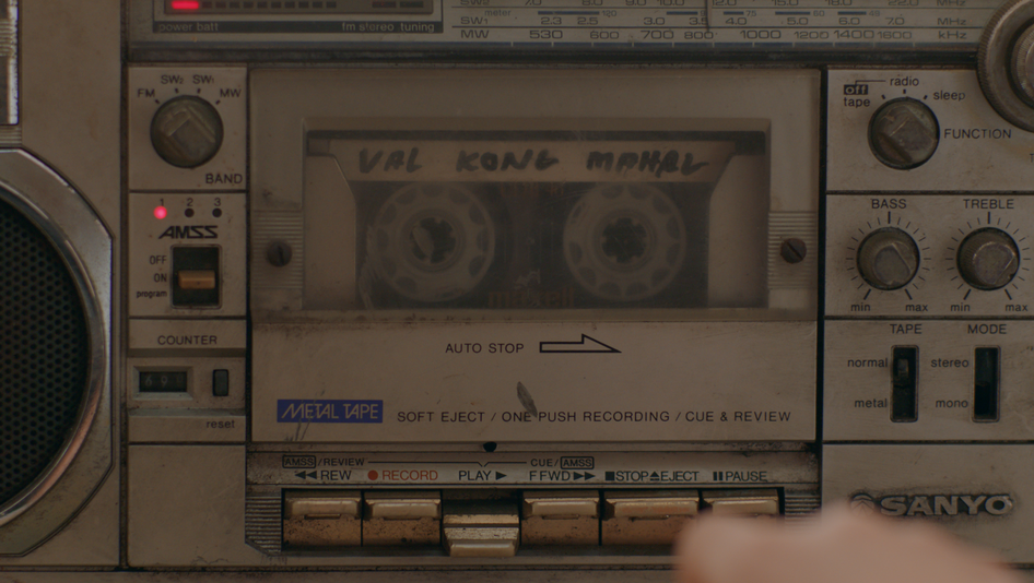 Filmstill aus NERVOUS TRANSLATION: Nahansicht eines sehr alten Kassettenrekorders, in dem gerade eine Kassette abgespielt wird.