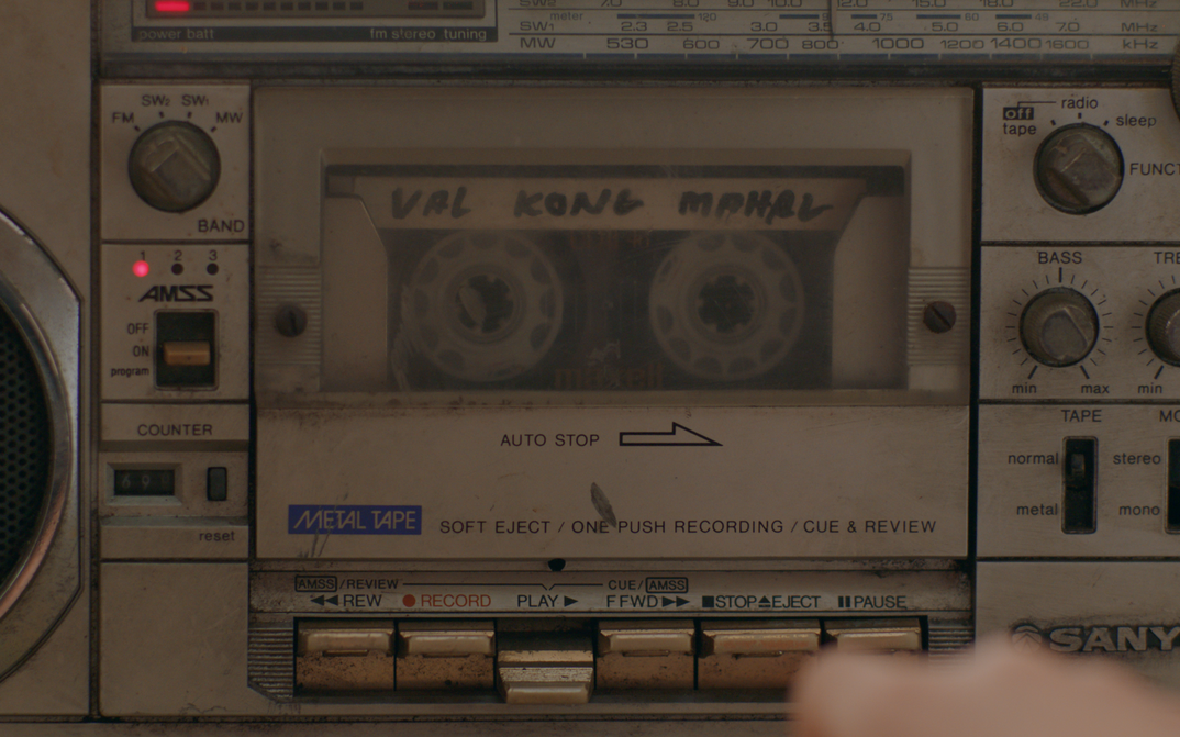 Filmstill aus NERVOUS TRANSLATION: Nahansicht eines sehr alten Kassettenrekorders, in dem gerade eine Kassette abgespielt wird.