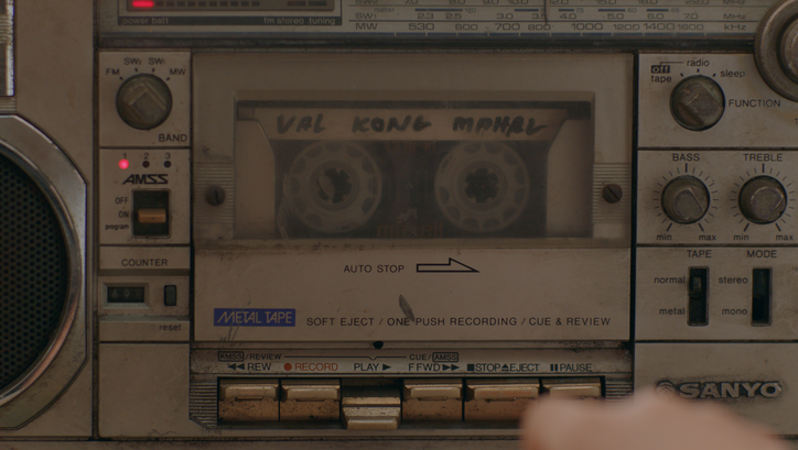 Film still from NERVOUS TRANSLATION: Close-up view of a very old cassette recorder in which a cassette is being played.