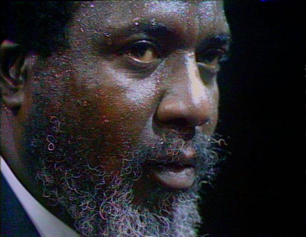 Filmstill aus „Rewind & Play“. Eine Nahaufnahme des Gesichts von Thelonious Monk. Es glänzt, sein Blick ist intensiv. Das Bild ist im Videoformat aufgenommen.