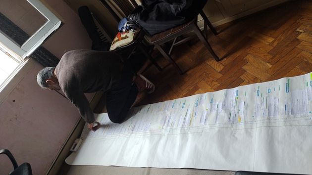 Ulises de la Orden analysing the structure of his film with a paper roll several meters long on the wooden floor of an apartment building, production photo of EL JUCIO (The Trial)