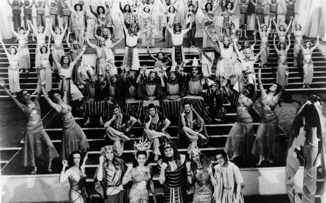 Film still from LA CORTE DE FARAÓN: A musical choreography on a show staircase, the performers in Egyptian costumes.