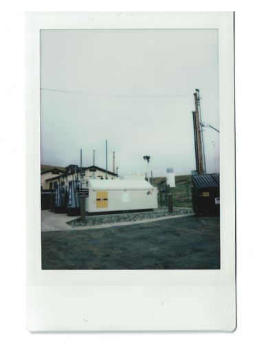 Polaroid elektrischer Anlagen an einem Haus neben einem Müllcontainer und einem Parkplatz.