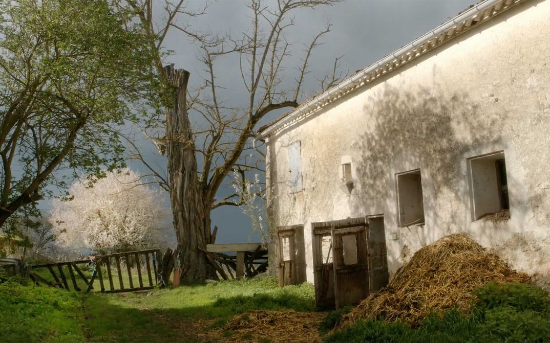 Filmstill aus DIE FABELHAFTE WELT DES DR. CADÉOT: Ein weiß getünchtes Stallgebäude mit Mist davor, man sieht auch Bäume und einen Zaun.