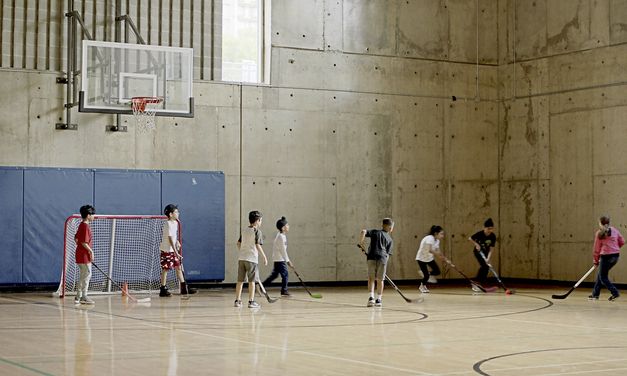 Filmstill from „Concrete Valley" by Antoine Bourges. Eight children play field hockey in a gymnasium.