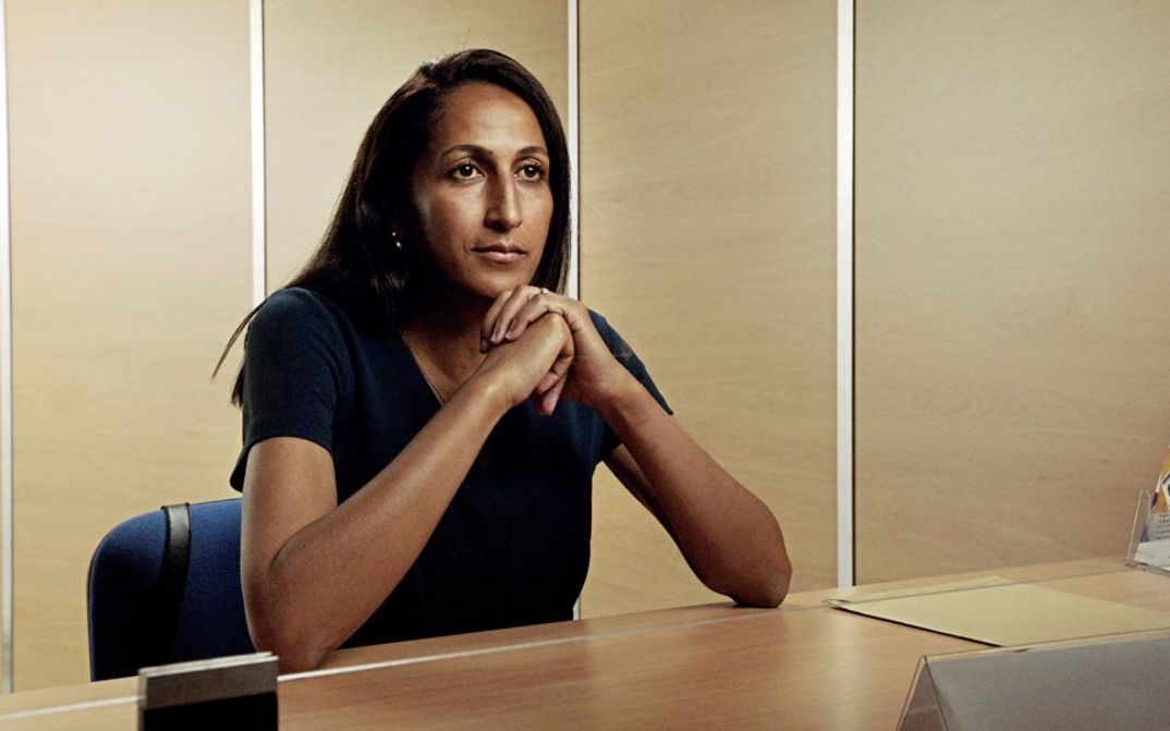 Still from the film "Europe" by Philipp Scheffner. A dark haired woman sits at a table with her elbows propped up.