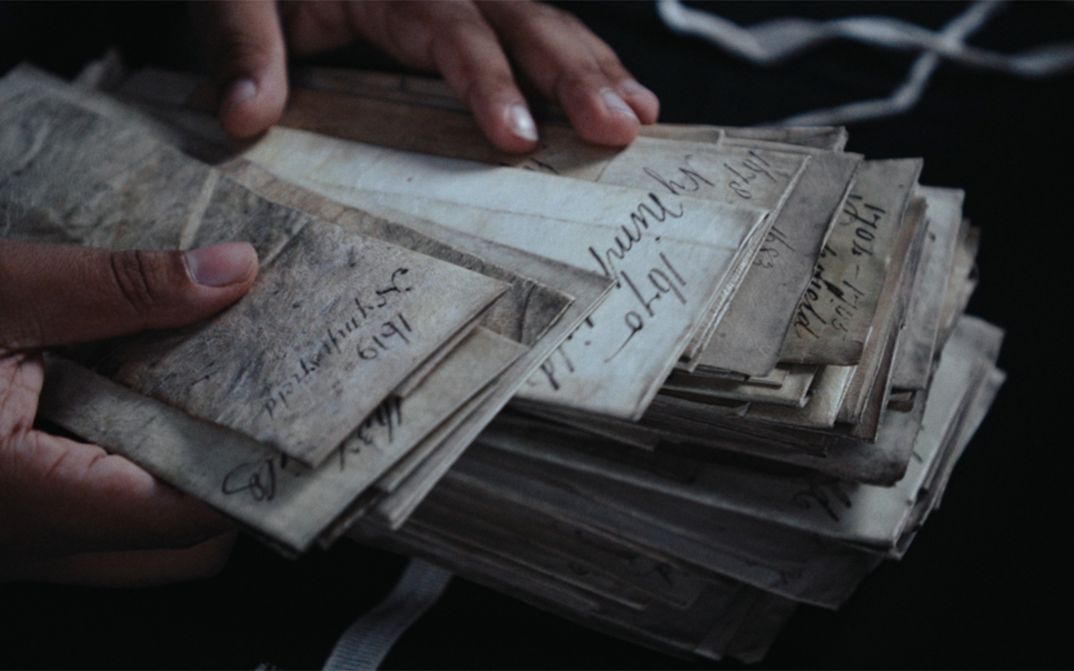 Film still from Dan Guthrie’s „Black Strangers“. Two Hands browse through a stack of faded documents. 