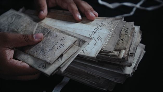 Film still from Dan Guthrie’s „Black Strangers“. Two Hands browse through a stack of faded documents. 