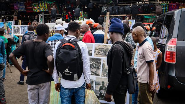 Filmstill aus dem Film "Kumbuka" von Petna Ndaliko Katondolo. Menschen auf einem Markt schauen sich Fotos an.