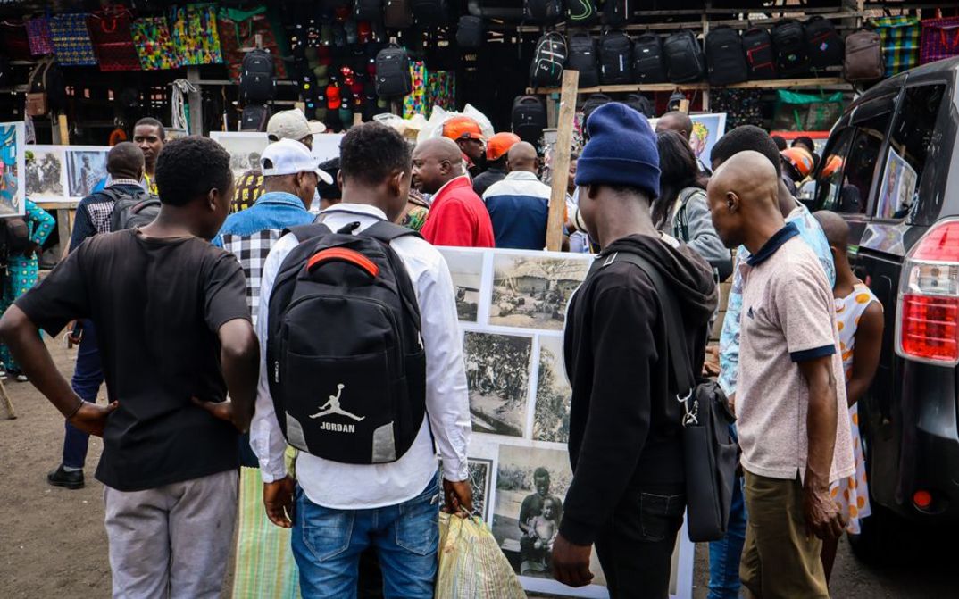 Still from the film "Kumbuka" by Petna Ndaliko Katondolo. People in a market look at photos.