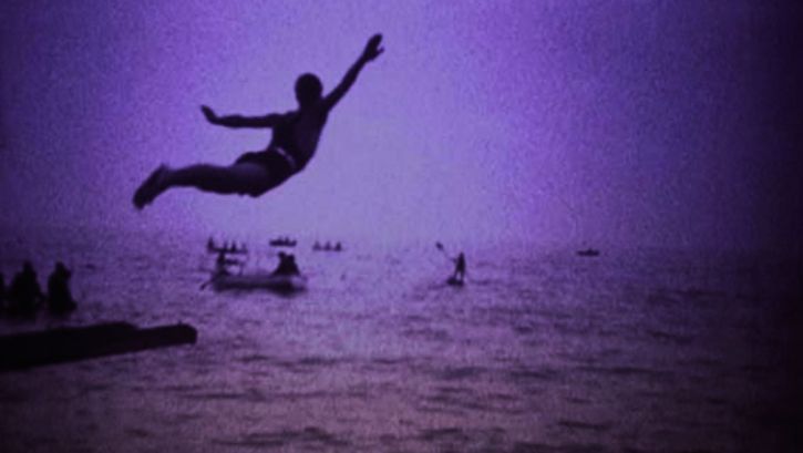 Film still from LA BOCCA DEL LUPO: Monochrome coloured image of a man jumping into the sea.