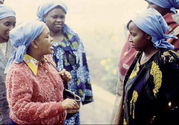 Still from the film „Der Kampf um den heiligen Baum" by Wanjiru Kinyanjui. One can see a total of five women. The woman on the left in the front is talking to the woman on the right in the front.