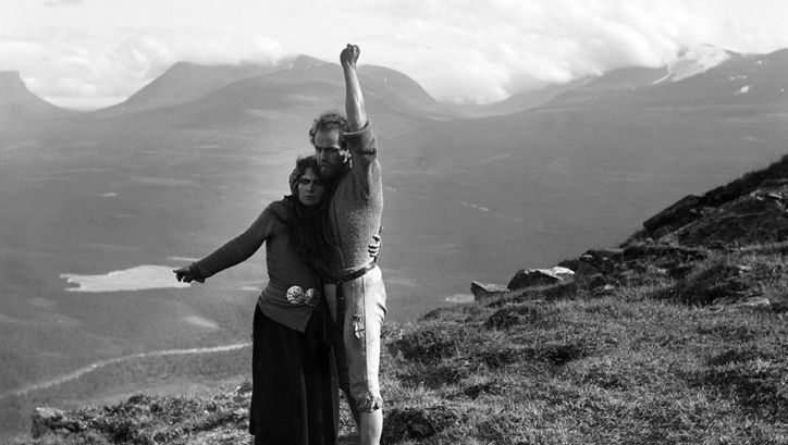 Film still from BERG-EYVIND AND HIS WIFE: A man and a woman stand in a lonely mountain landscape. They are holding each other and each has one arm stretched out from them. 