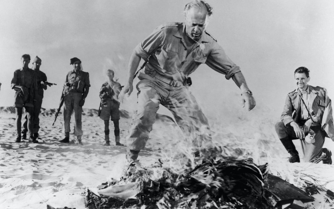Film still from BITTER VICTORY: A few men in military uniforms in the desert stand around a fire.
