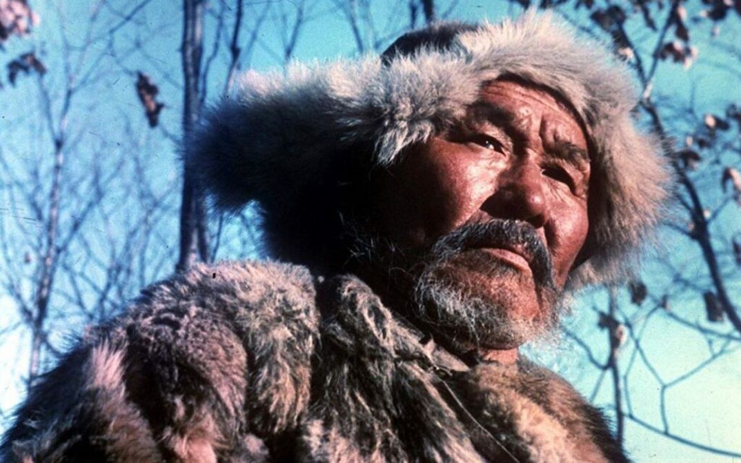 Filmstill aus DERSU UZALA: Ein in Fellmütze und -jacke gekleideter Jäger vor blauem Himmel.