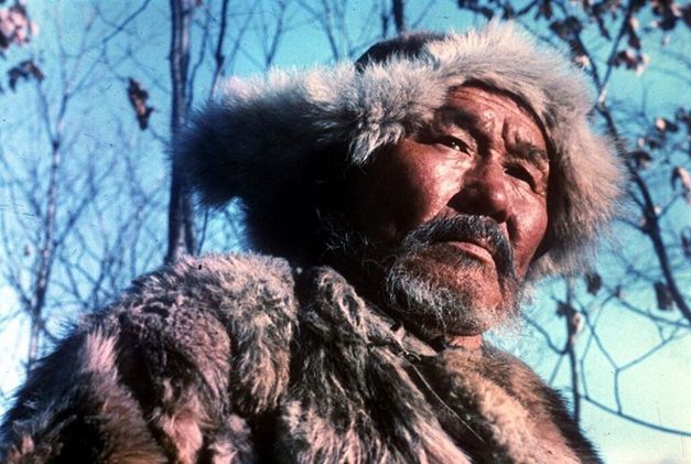 Film still from DERSU UZALA: A hunter dressed in fur cap and jacket in front of blue sky.