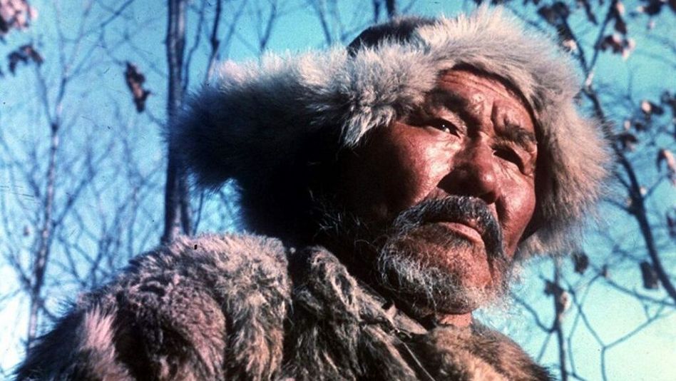Film still from DERSU UZALA: A hunter dressed in fur cap and jacket in front of blue sky.
