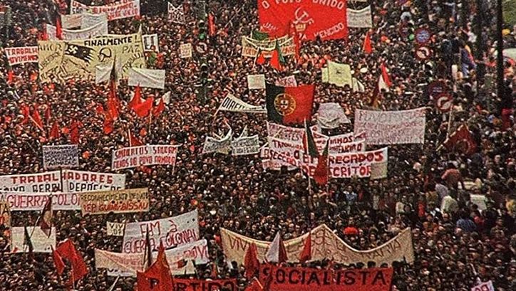 Filmstill aus AS ARMAS E O POVO: Man sieht die Menschenmenge einer riesigen Demonstration. Viele haben große Banner oder Fahnen dabei.
