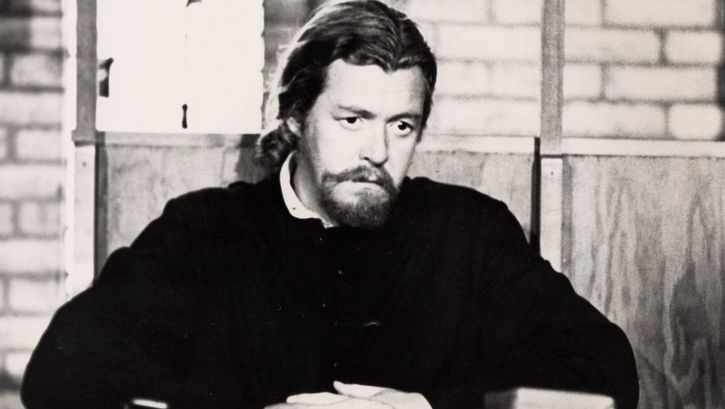 Film still from ESSENE. A monk is sitting at a table with a book in front of him.