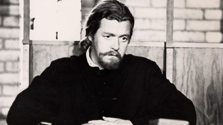 Film still from ESSENE. A monk is sitting at a table with a book in front of him.