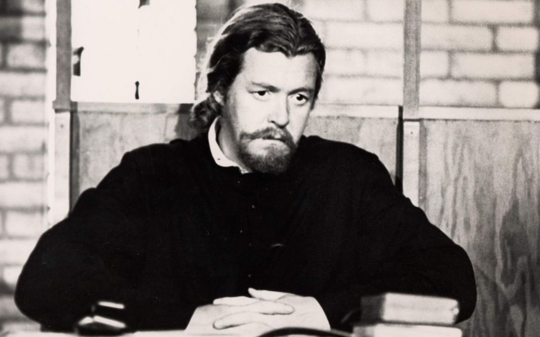 Film still from ESSENE. A monk is sitting at a table with a book in front of him.