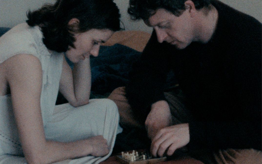 Filmstill aus NEBELLAND: Eine Frau und ein Mann beugen sich über ein Schachspiel zwischen ihnen.