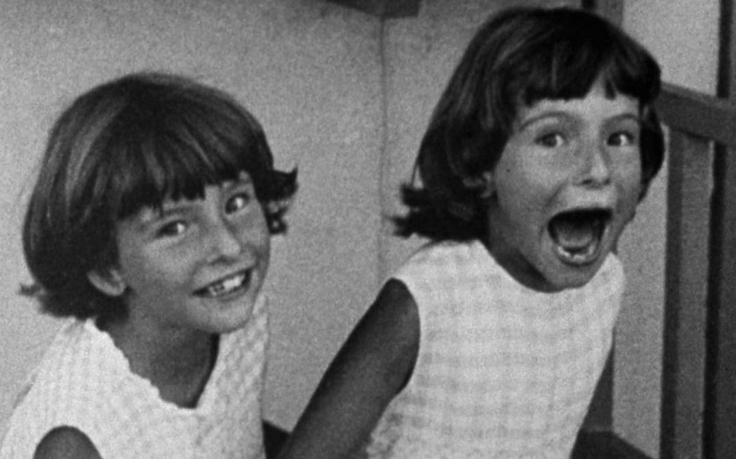 Film still from POTO AND CABENGO: Two twin girls laugh into the camera, one has her mouth wide open.