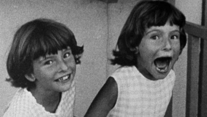 Film still from POTO AND CABENGO: Two twin girls laugh into the camera, one has her mouth wide open.