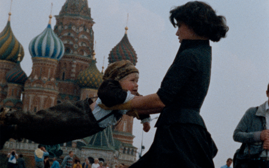 Film still from OH! DIE VIER JAHRESZEITEN. A woman swings a child against the background of St. Basil