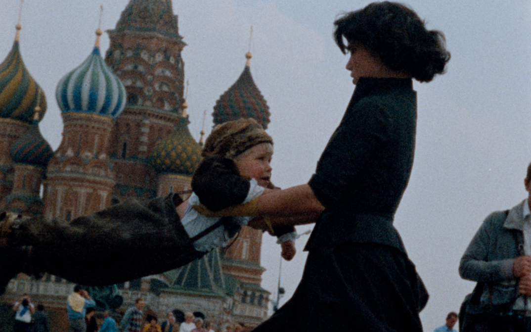 Film still from OH! DIE VIER JAHRESZEITEN. A woman swings a child against the background of St. Basil