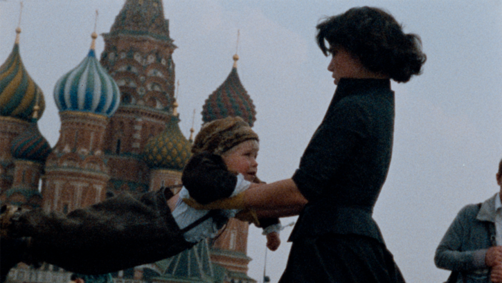 Film still from OH! DIE VIER JAHRESZEITEN. A woman swings a child against the background of St. Basil