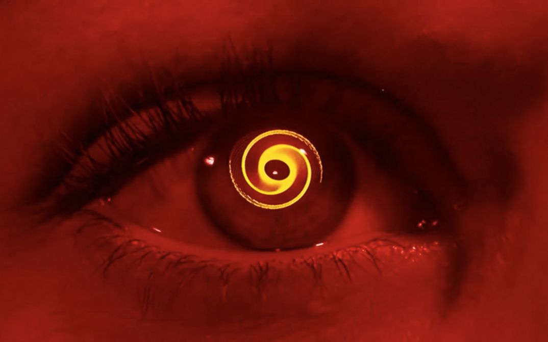 Film still from VERTIGO: Monochrome red colored close-up of an eye, a spiral turns in the pupil.