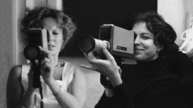 Film still from DELPHINE ET CAROLE, INSOUMUSES: Two women each hold a small film camera and look through the viewfinder.
