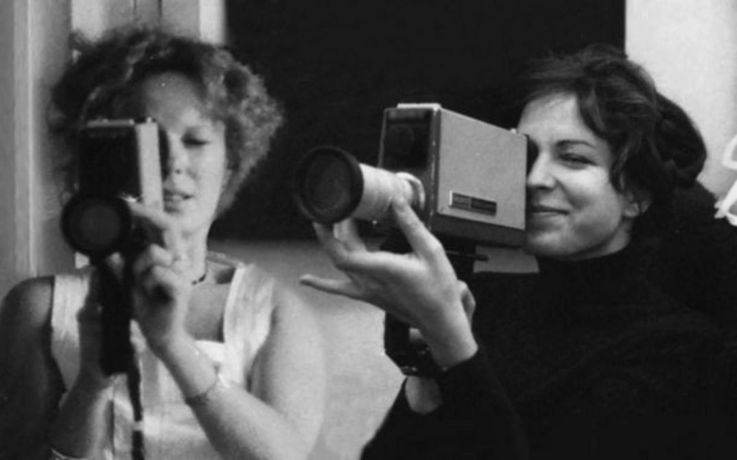 Film still from DELPHINE ET CAROLE, INSOUMUSES: Two women each hold a small film camera and look through the viewfinder.