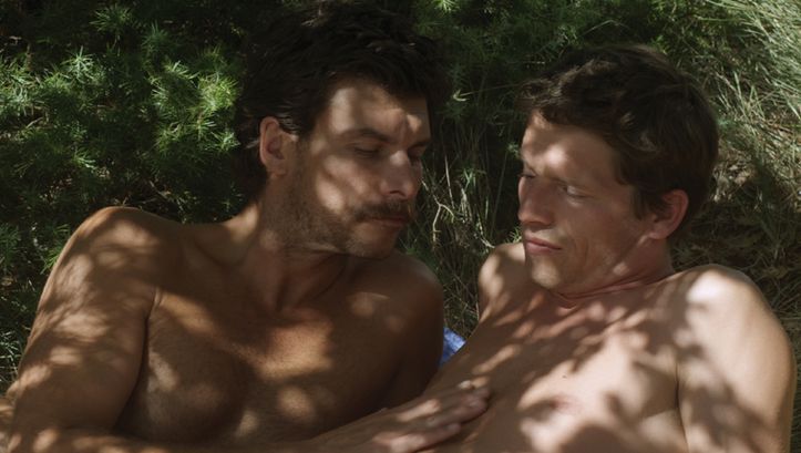 Film still from L’INCONNU DU LAC: Two men are lying in the grass.