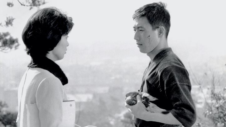 Filmstill aus KEN: Ein Mann und eine Frau blicken sich an. Er trägt einen Kimono und hält einen verletzten Vogel in seinen Händen.