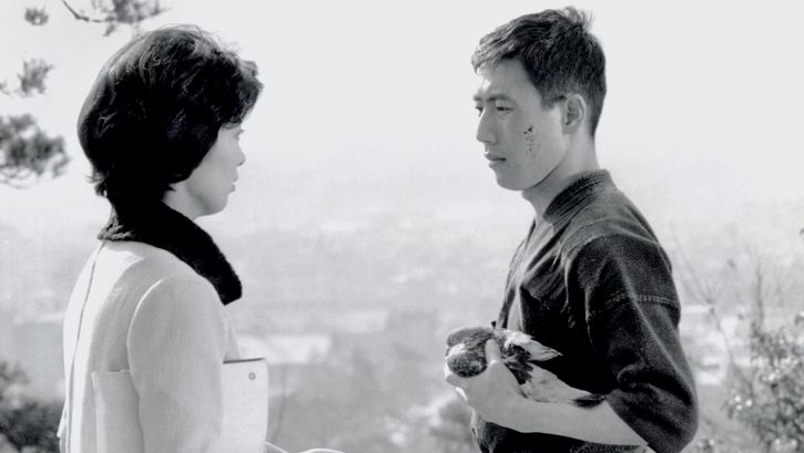 Film still from KEN: A man and a woman look at each other. He is wearing a kimono and holding an injured bird in his hands.